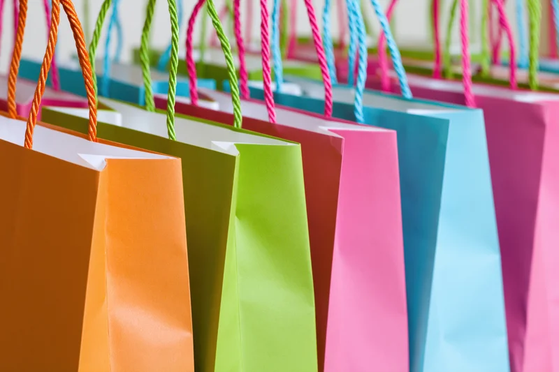 Colorful paper shopping bags standing upright in a row, arranged side by side, showcasing vibrant hues and twisted handles