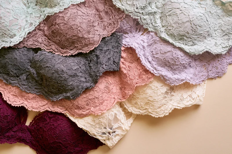 Multiple lace bras in various colors arranged overlapping on a beige surface