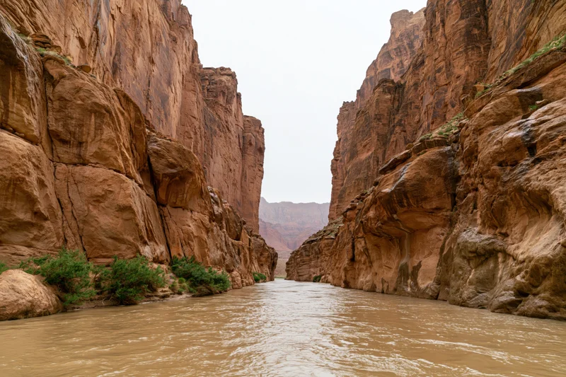 Muddy river flowing through narrow desert canyon with towering sandstone cliffs