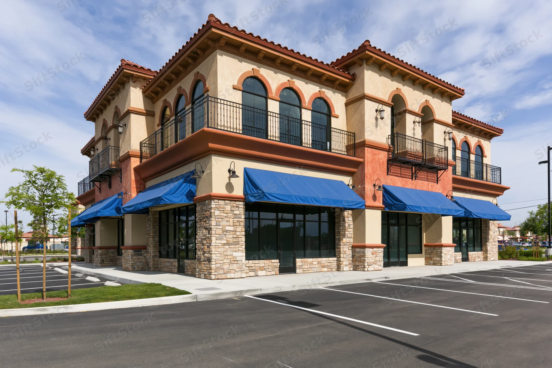Two-story mediterranean-style strip mall with blue awnings and stone facade overlooking a parking lot