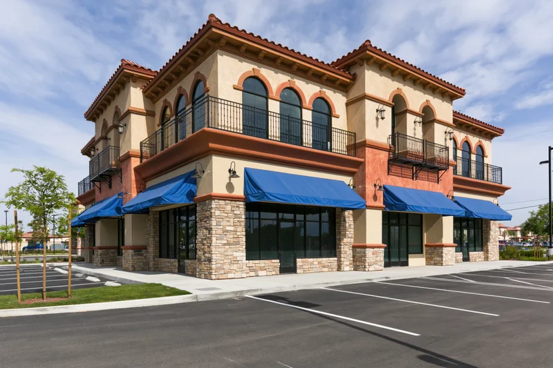 Two-story mediterranean-style strip mall with blue awnings and stone facade overlooking a parking lot
