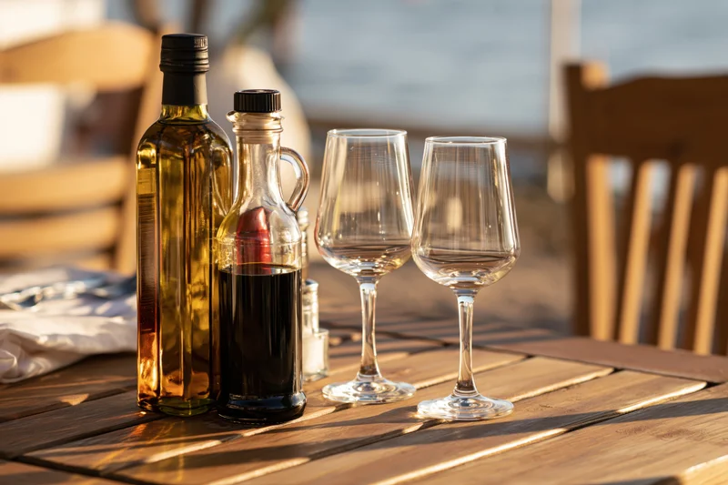 Olive oil and vinegar bottles with empty wine glasses on a wooden table by the seaside