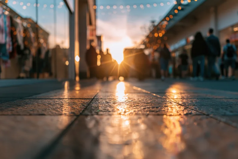 Low-angle view of wet pavement reflecting golden sunset light along a pedestrian shopping street at dusk