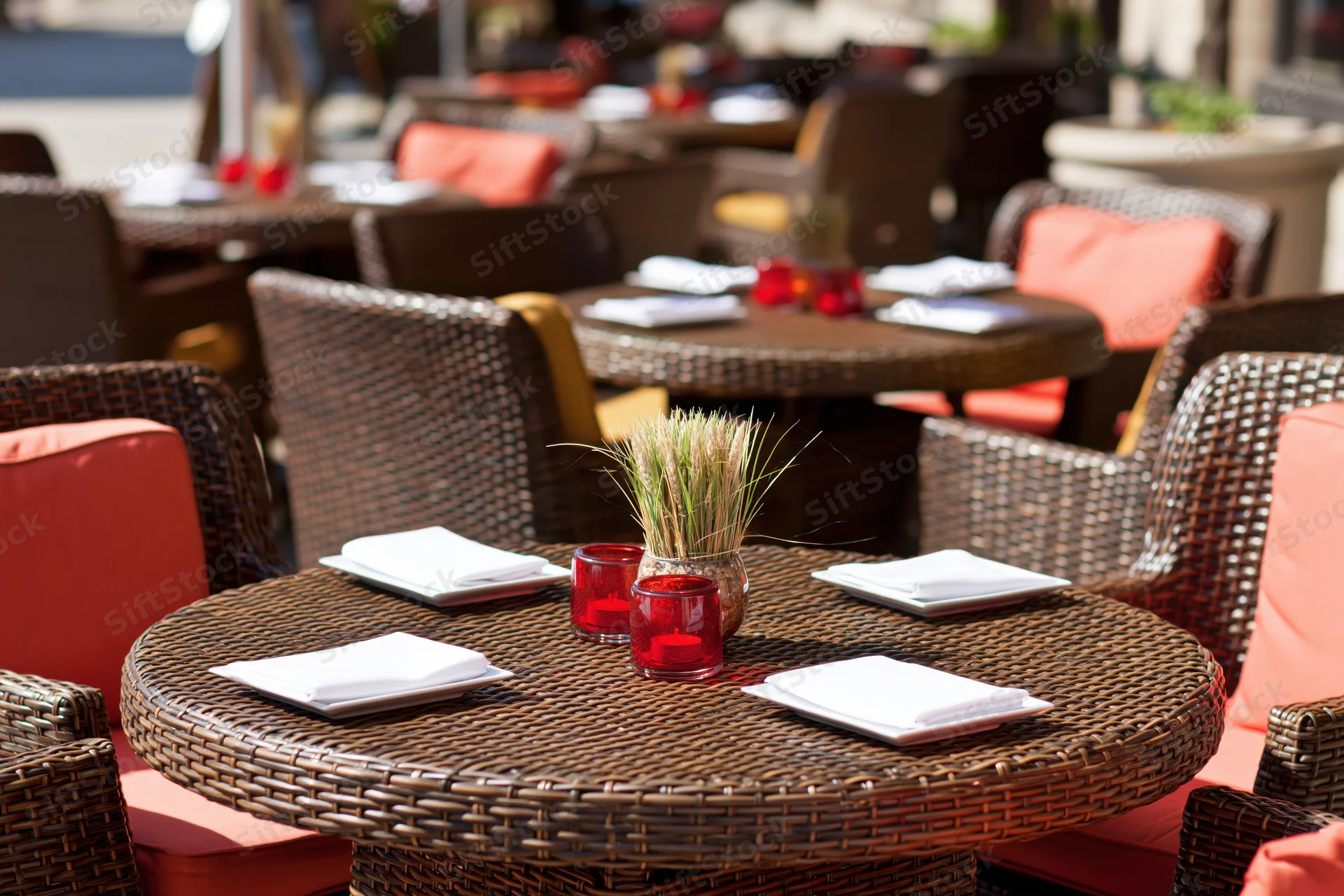 Round wicker table set for dining on an outdoor restaurant terrace with orange cushions and centerpiece