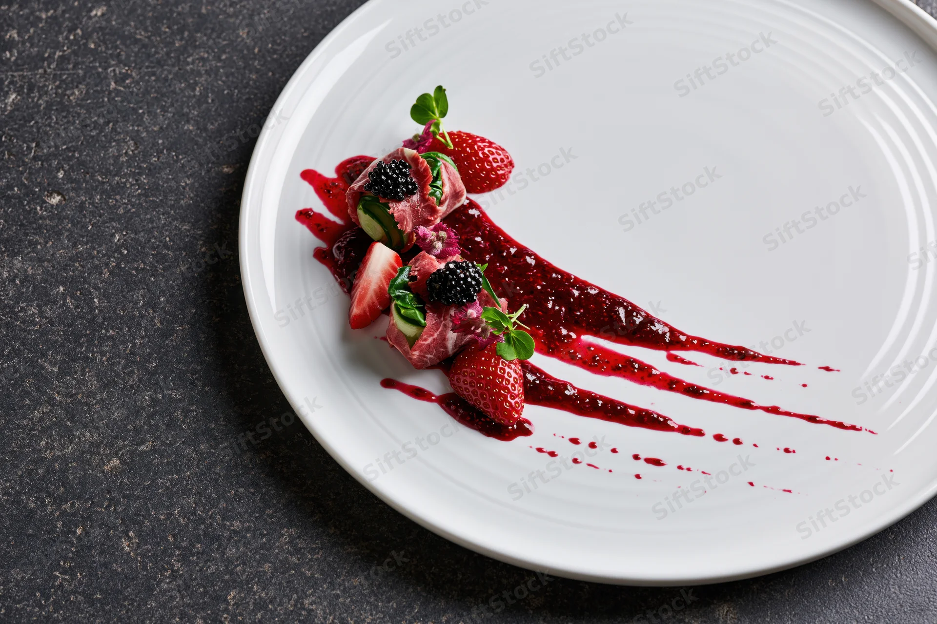 Fine dining appetizer with berry sauce and fruit garnish on white plate over dark surface