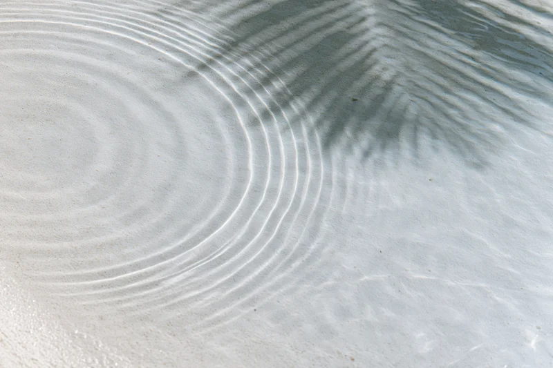 Shallow clear water over white sand with ripples and palm shadow from above