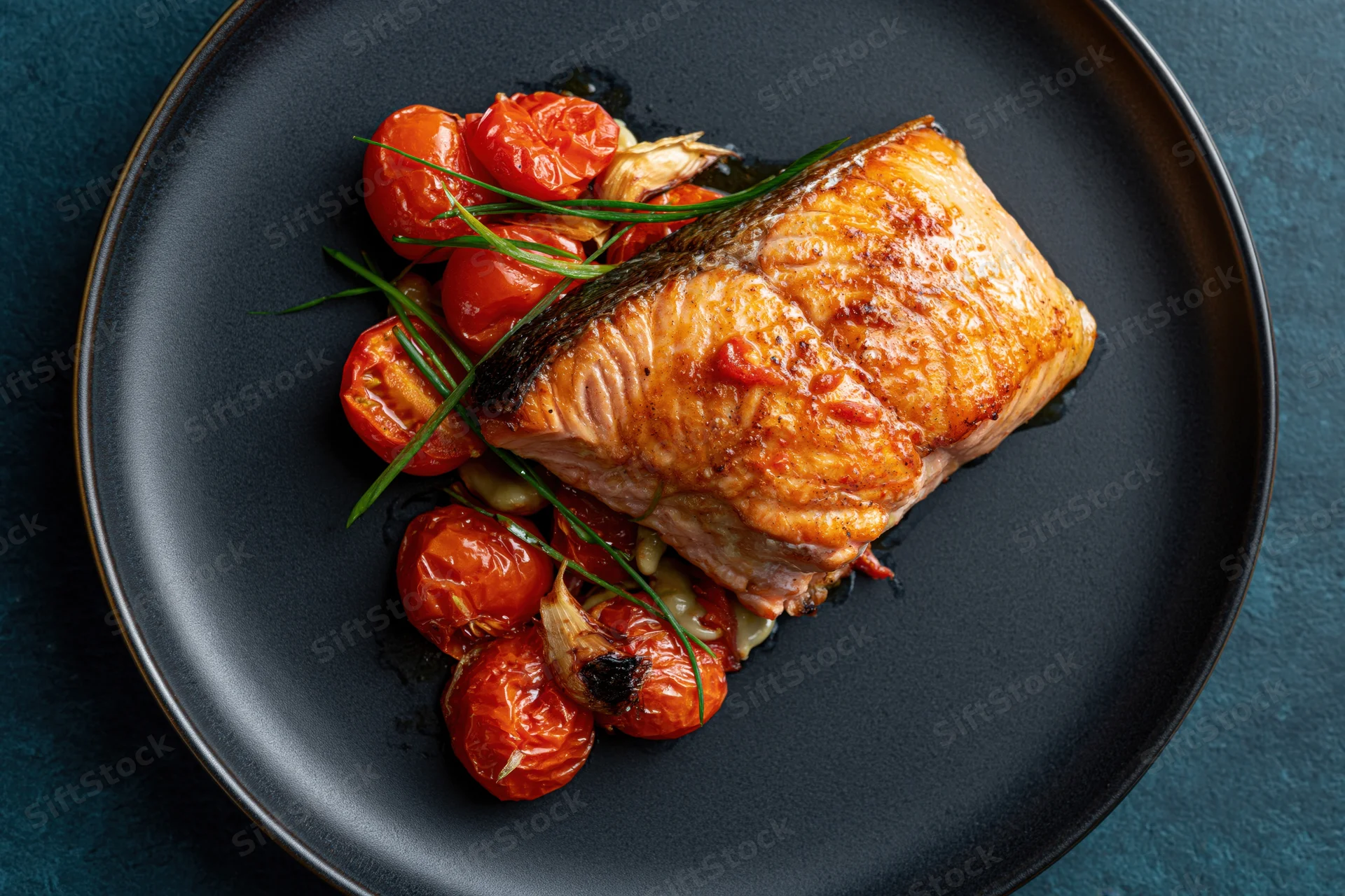 Pan-seared salmon fillet with roasted tomatoes and herbs on a dark matte ceramic plate