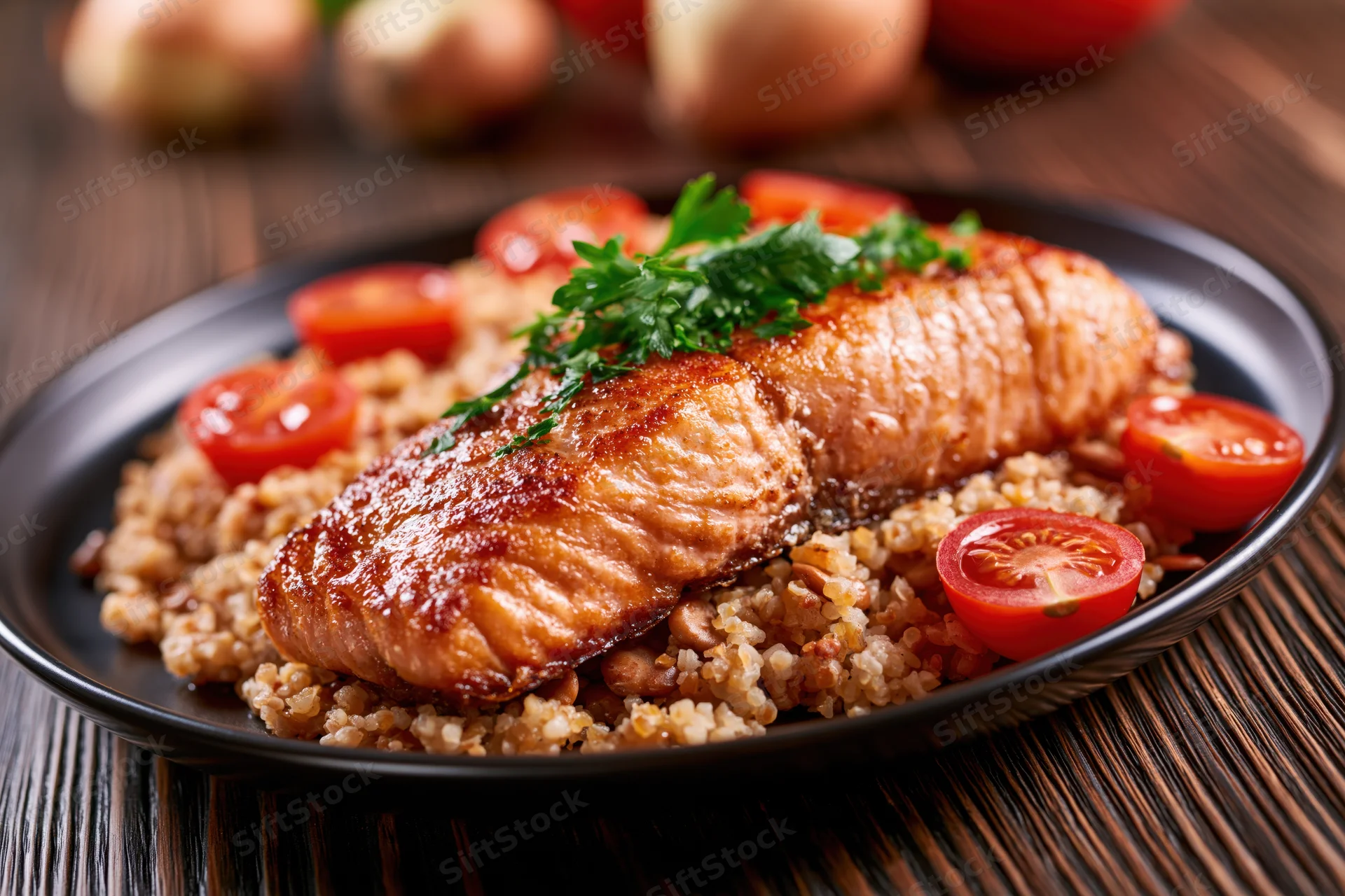 Pan-seared salmon fillet with golden-brown crust served on quinoa with cherry tomatoes and parsley on a black plate
