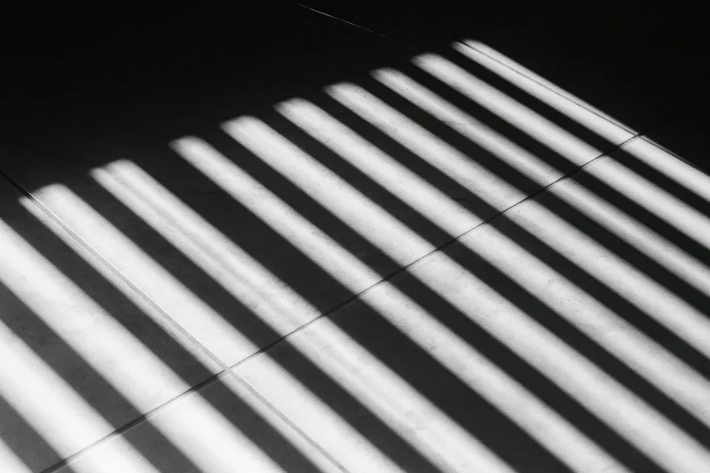 Parallel light stripes from venetian blinds cast on a tiled floor in a dark interior