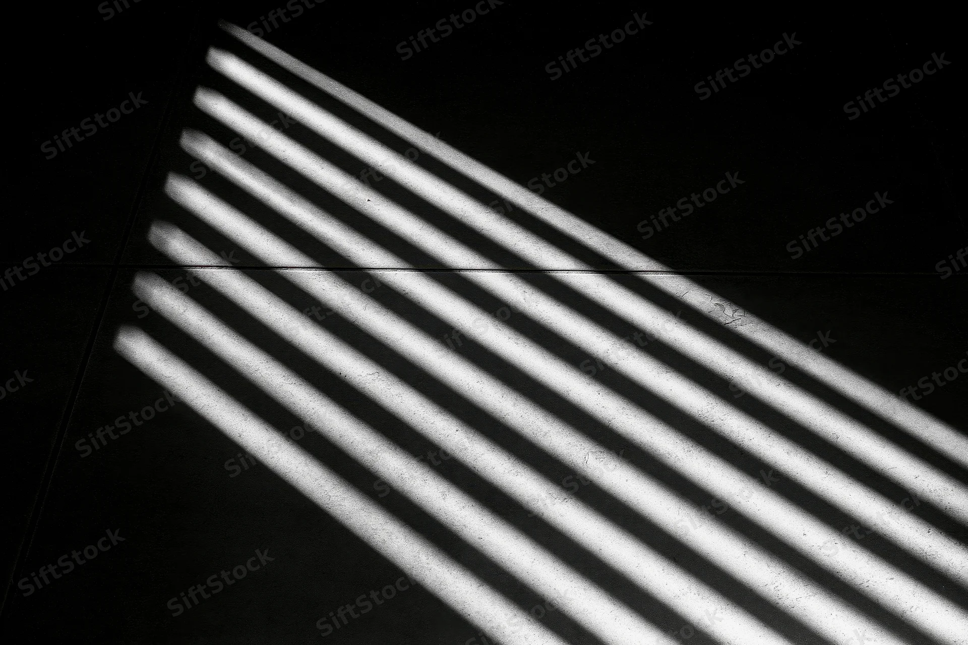 Parallel light stripes cast through venetian blinds on a concrete floor