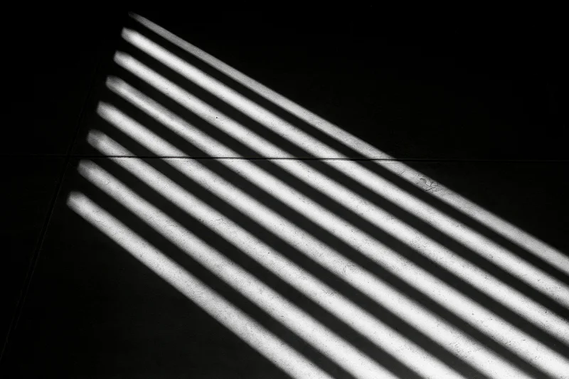 Parallel light stripes cast through venetian blinds on a concrete floor