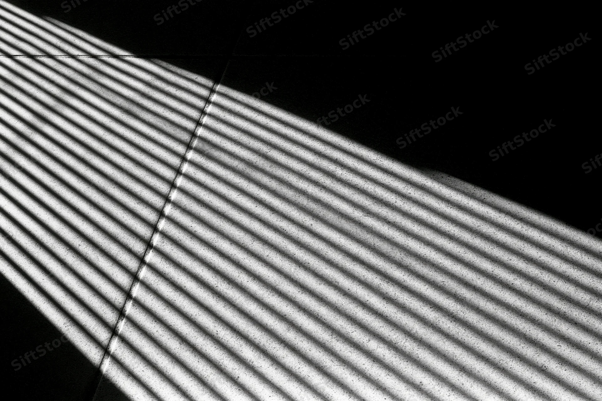 Parallel light stripes cast through venetian blinds on a tiled floor