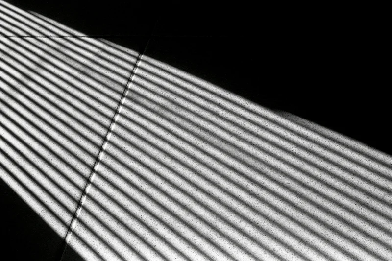 Parallel light stripes cast through venetian blinds on a tiled floor