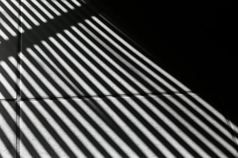 Parallel light stripes cast through venetian blinds on a tiled floor