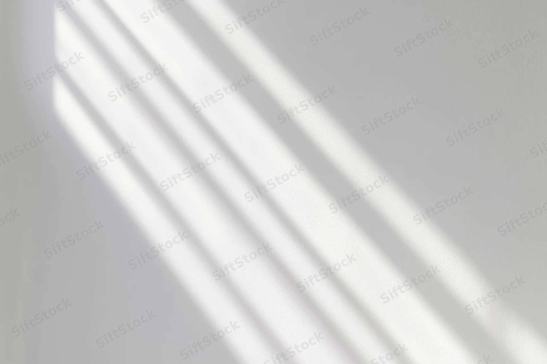 Diagonal light and shadow stripes on a white wall surface from a window