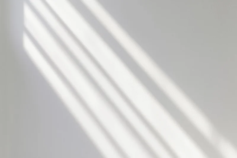 Diagonal light and shadow stripes on a white wall surface from a window
