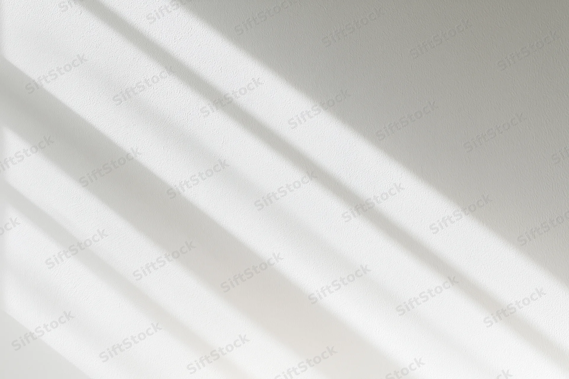 Diagonal light and shadow stripes on a white wall surface indoors