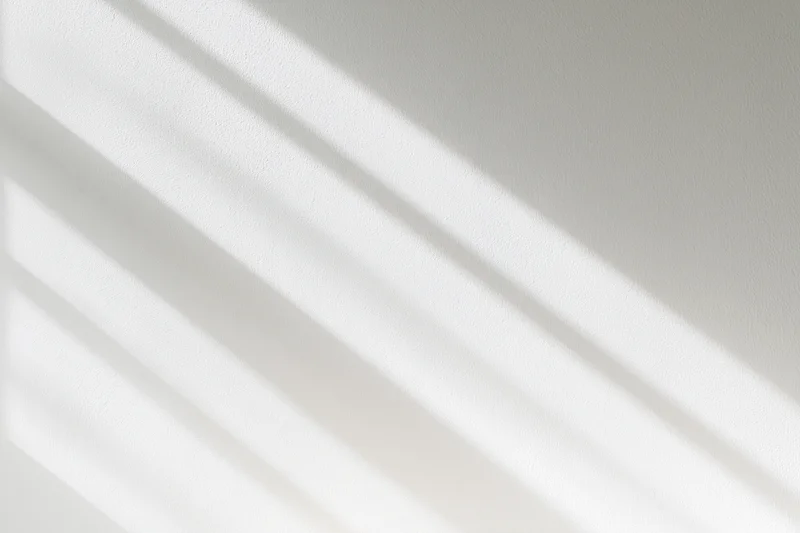 Diagonal light and shadow stripes on a white wall surface indoors