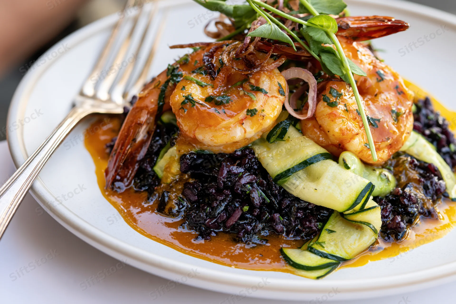 Sauteed shrimp over black rice with zucchini and herbs on a white plate with a fork beside it