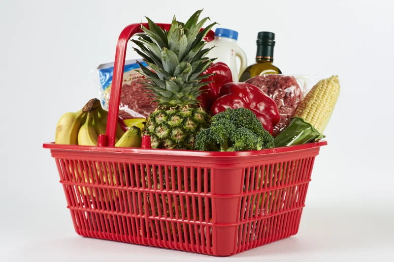 Red plastic shopping basket filled with fresh groceries including fruits vegetables meat and dairy products