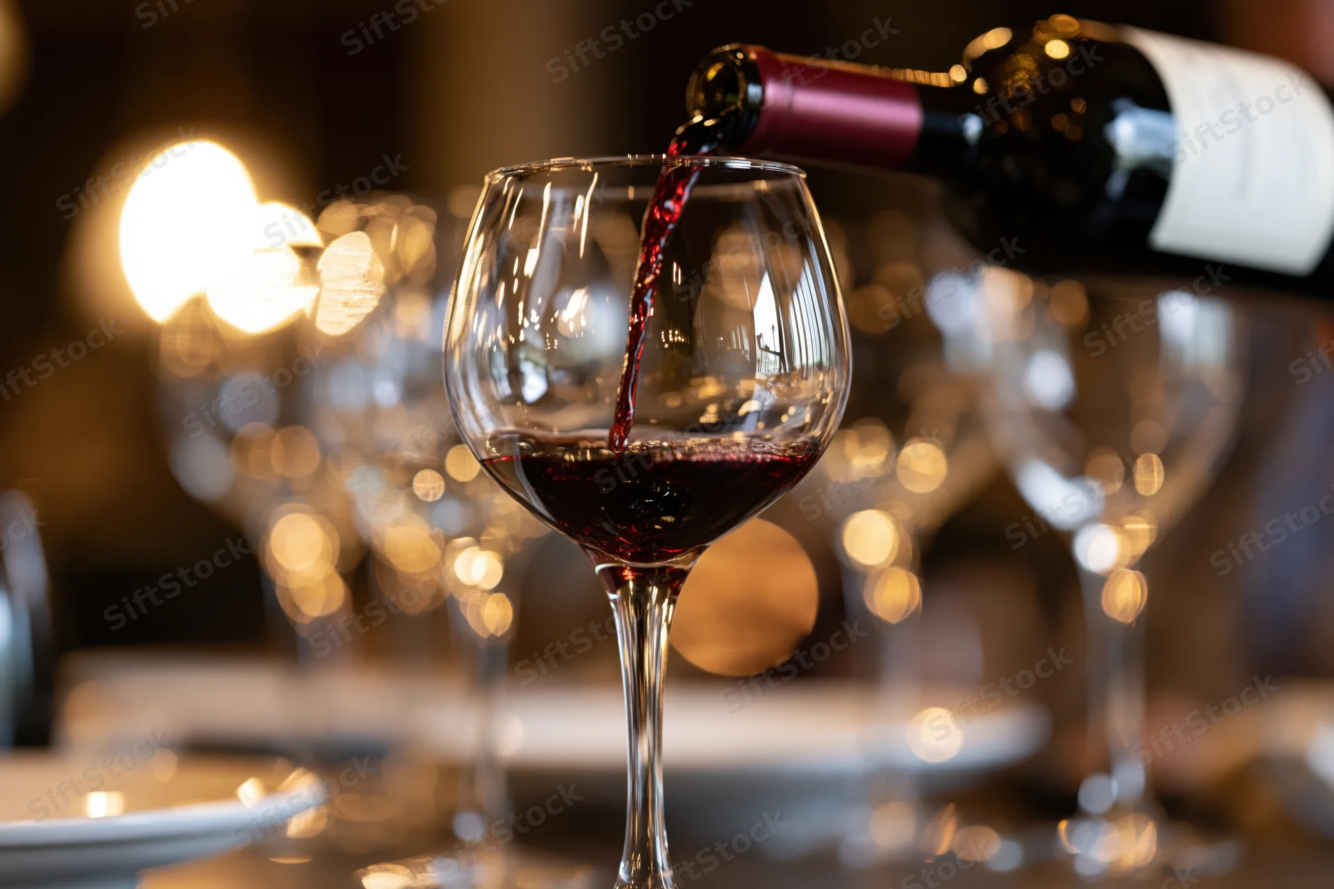 Red wine being poured from a bottle into a crystal wine glass on a dining table in a restaurant setting