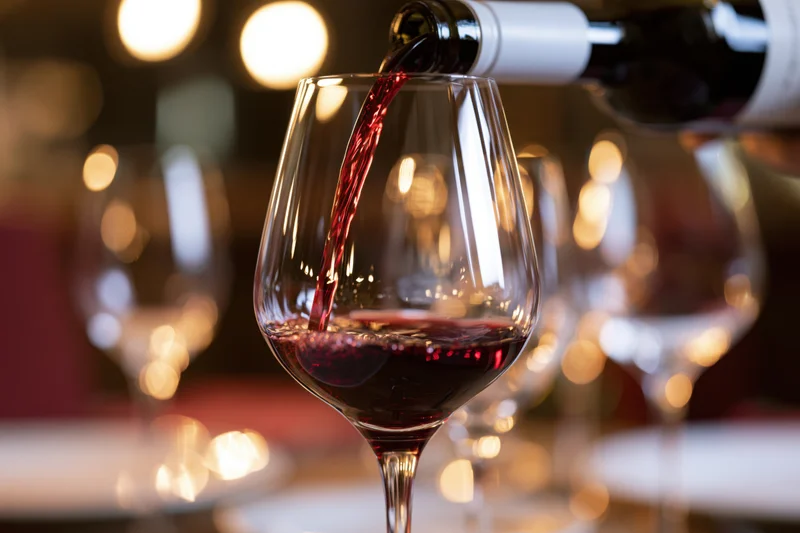 Red wine being poured from a bottle into a crystal wine glass at a dining table
