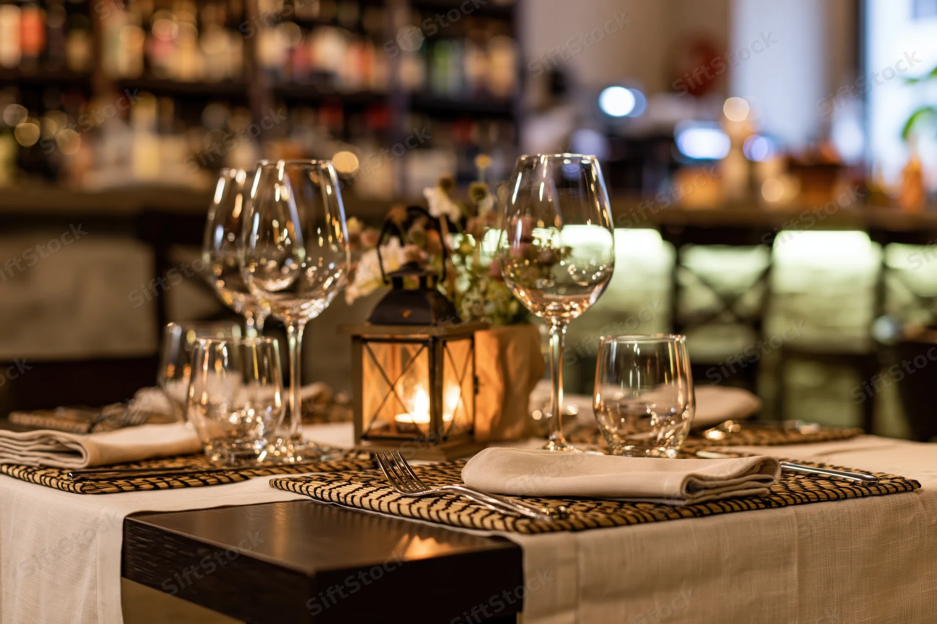 Dining table set for service with empty wine glasses and candlelit lantern in restaurant interior