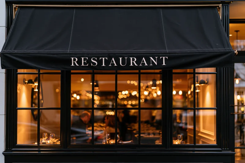 Restaurant storefront at night with black fabric awning and warm interior lights visible through glass windows