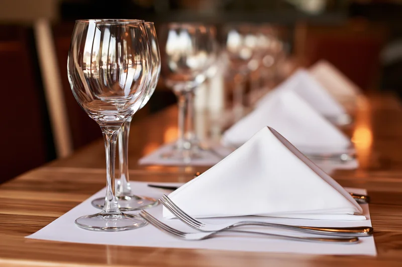 Formally set restaurant table with folded white linen napkins and glassware on wooden surface