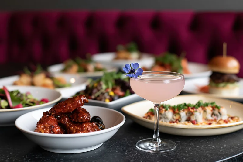 Restaurant table with multiple dishes and a cocktail garnished with a blue flower