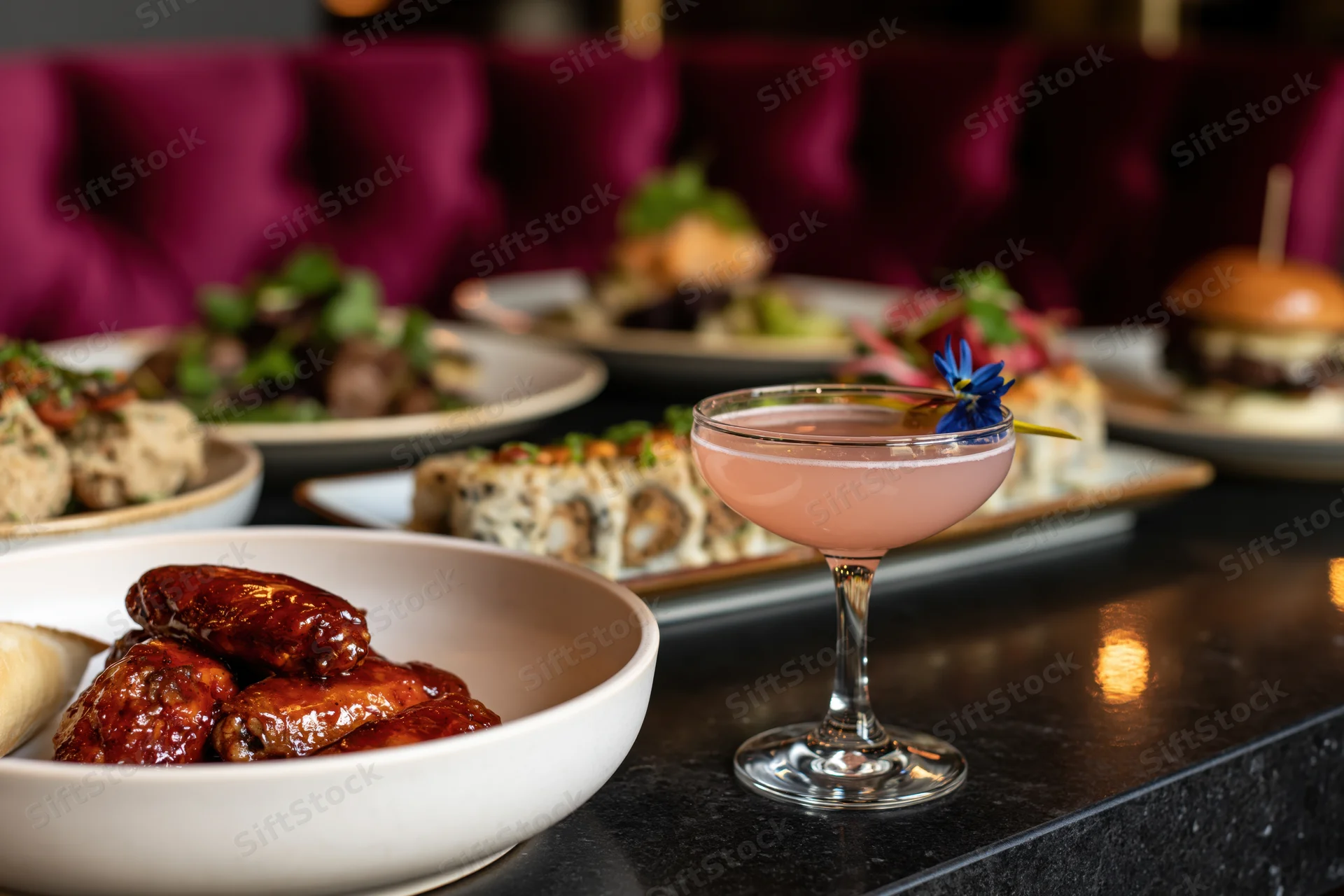 Restaurant table with glazed chicken wings, cocktail, and assorted dishes arranged on a marble counter