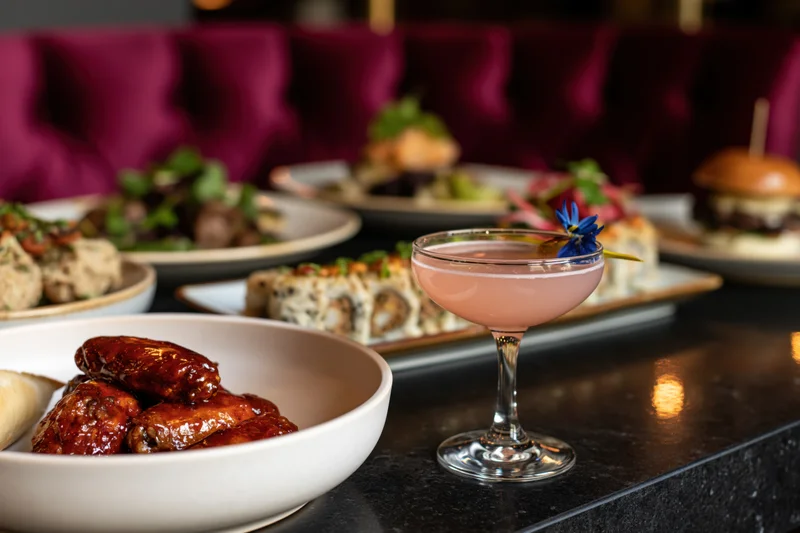 Restaurant table with glazed chicken wings, cocktail, and assorted dishes arranged on a marble counter