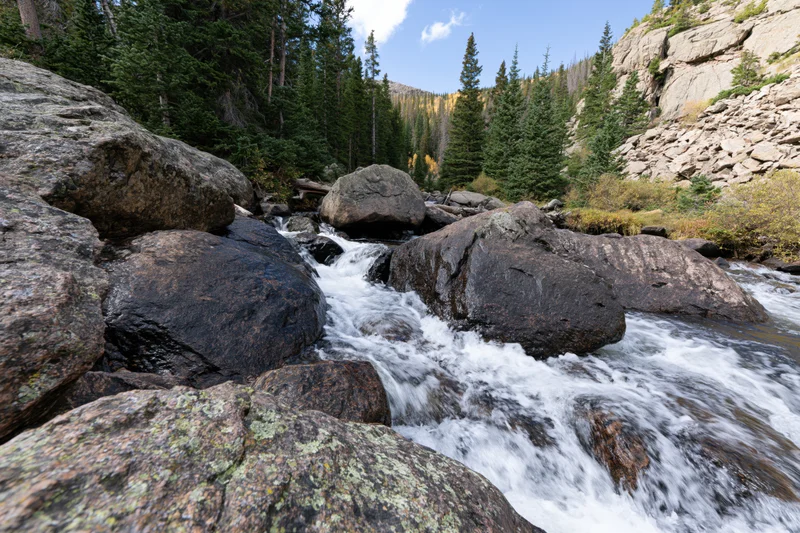 Mountain stream rushing over large boulders through a forested valley