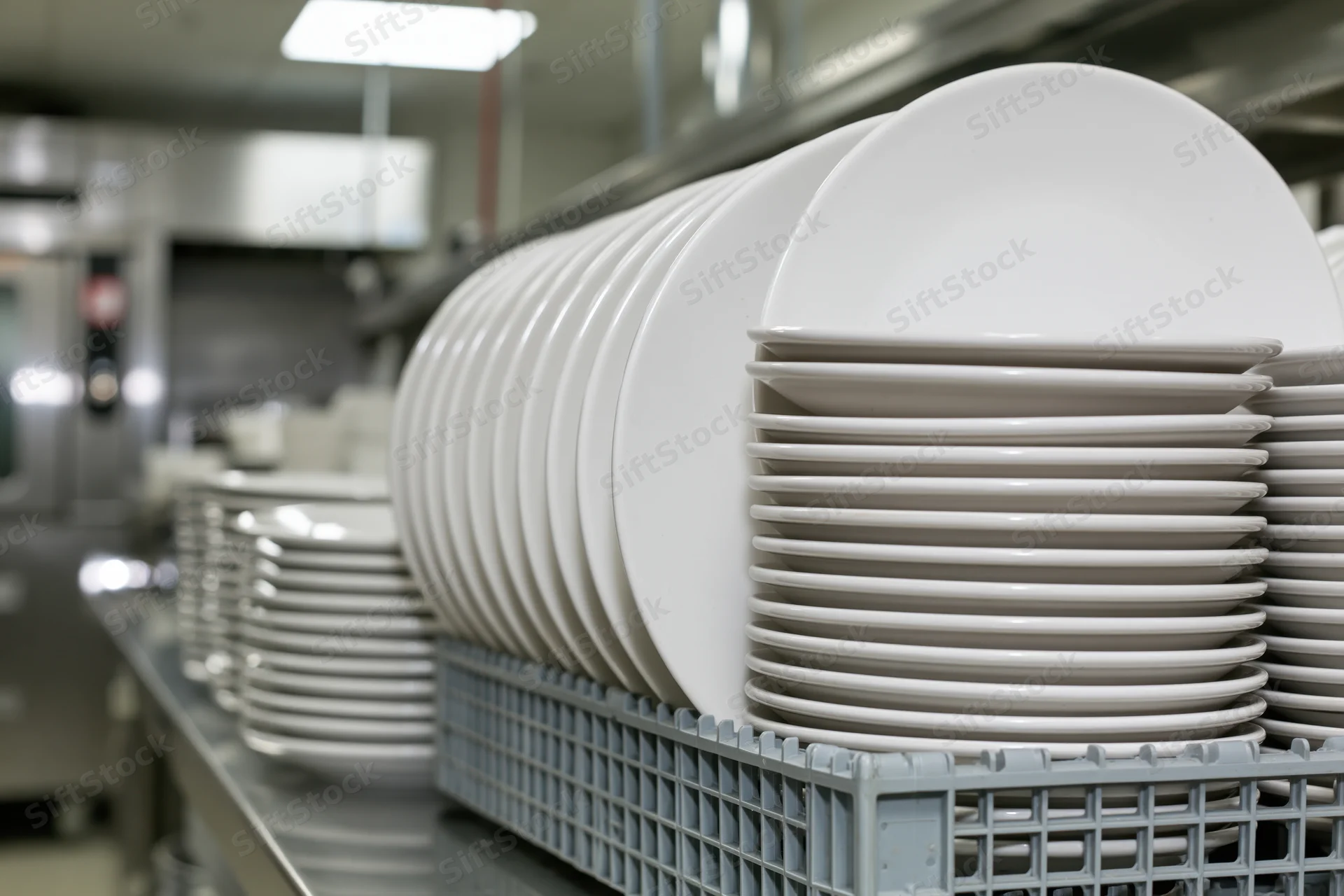 Stacks of clean white ceramic dinner plates arranged in a gray plastic rack in a commercial kitchen
