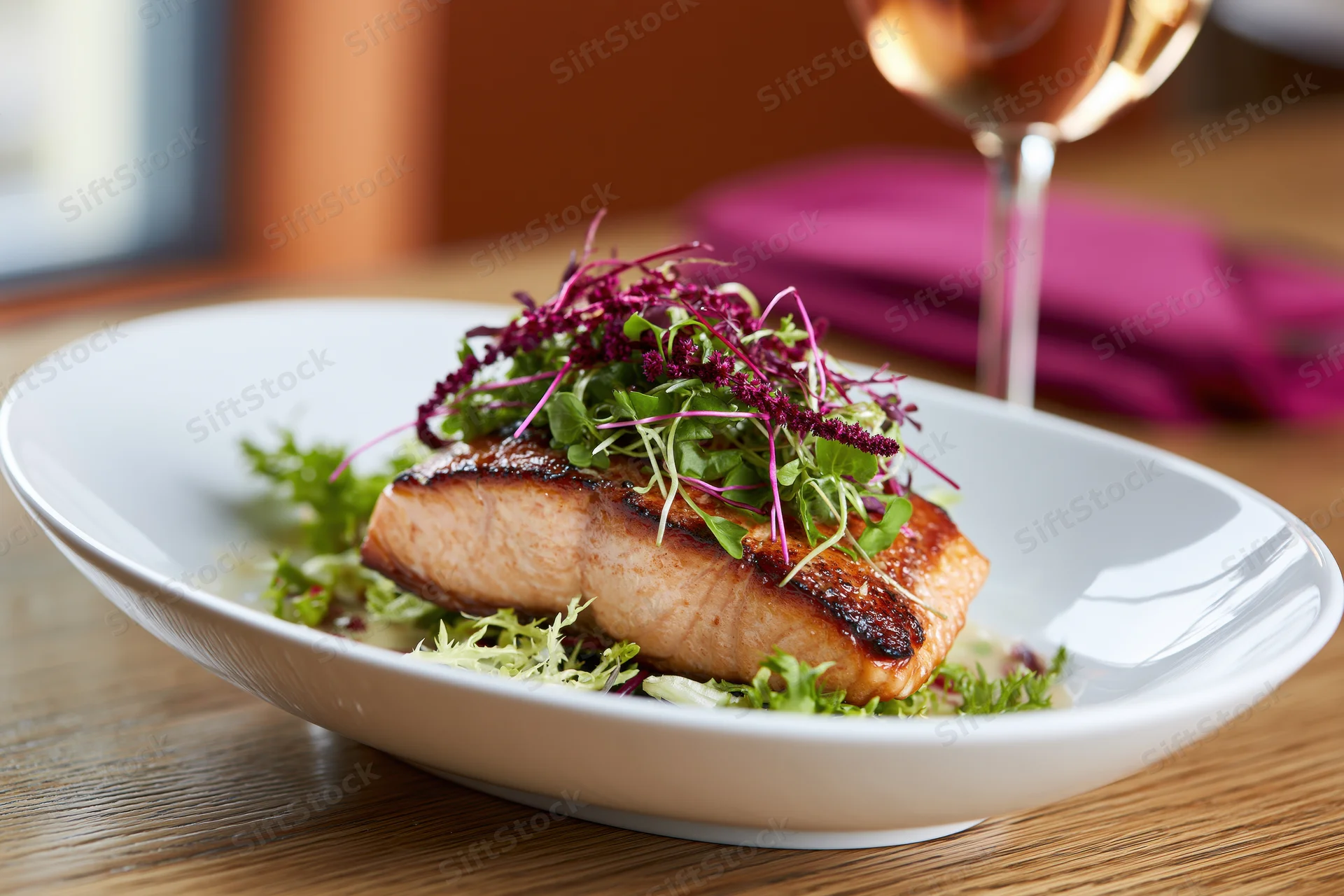 Seared salmon fillet topped with microgreens and red amaranth on a white plate at a dining table