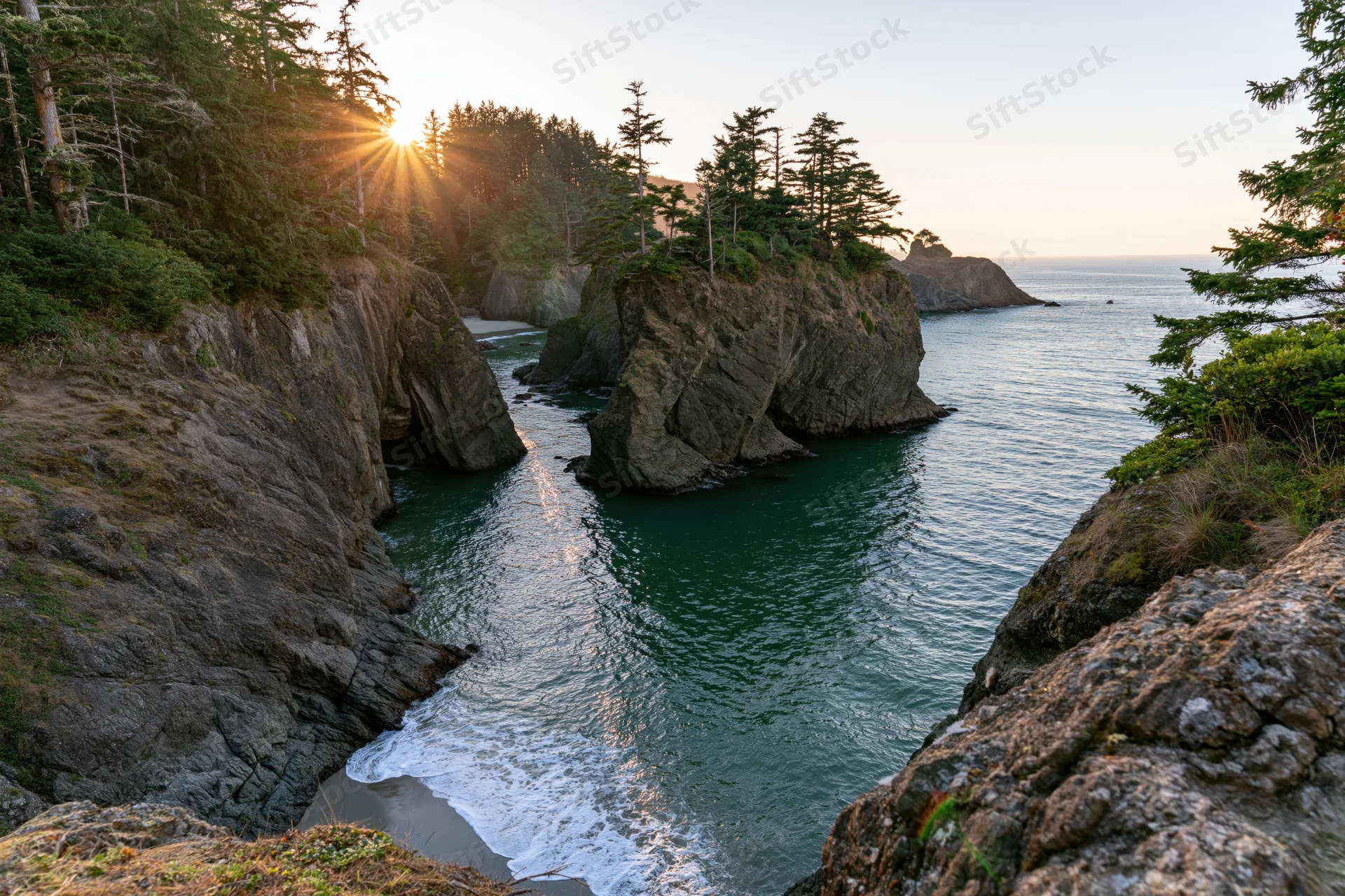 Secluded cove with rocky cliffs and evergreen trees overlooking the ocean at sunset