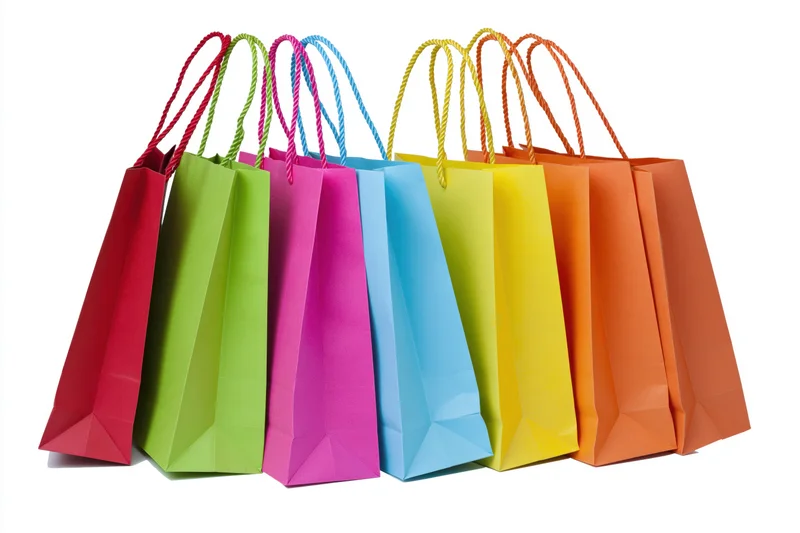 Seven colorful paper shopping bags with twisted rope handles arranged in a row on white background