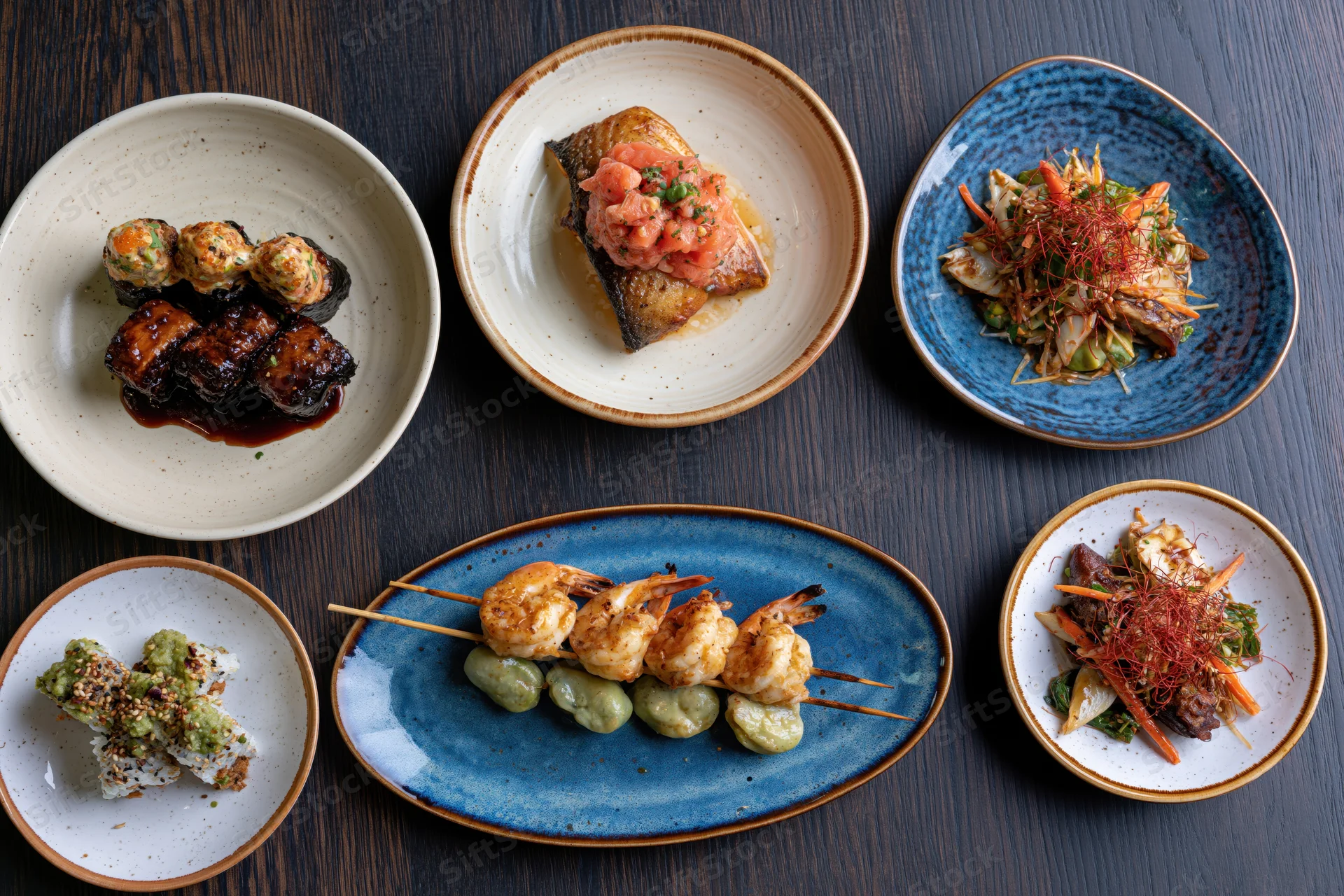 Seven restaurant dishes arranged on dark wooden table in overhead flatlay view