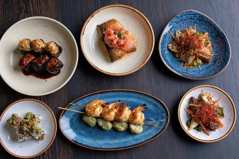 Seven restaurant dishes arranged on dark wooden table in overhead flatlay view
