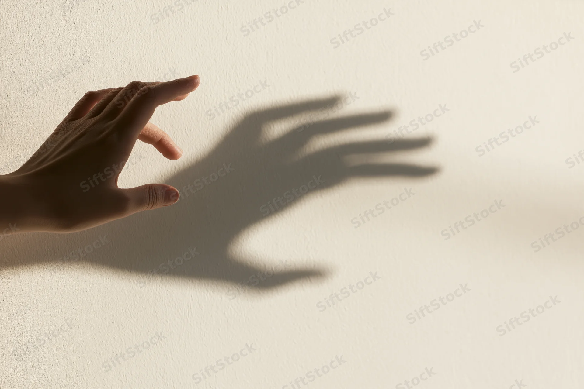 Hand casting a shadow on a plain off-white wall, fingers extended in a reaching gesture
