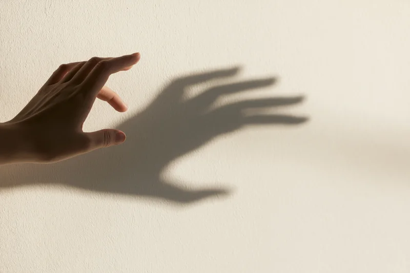 Hand casting a shadow on a plain off-white wall, fingers extended in a reaching gesture