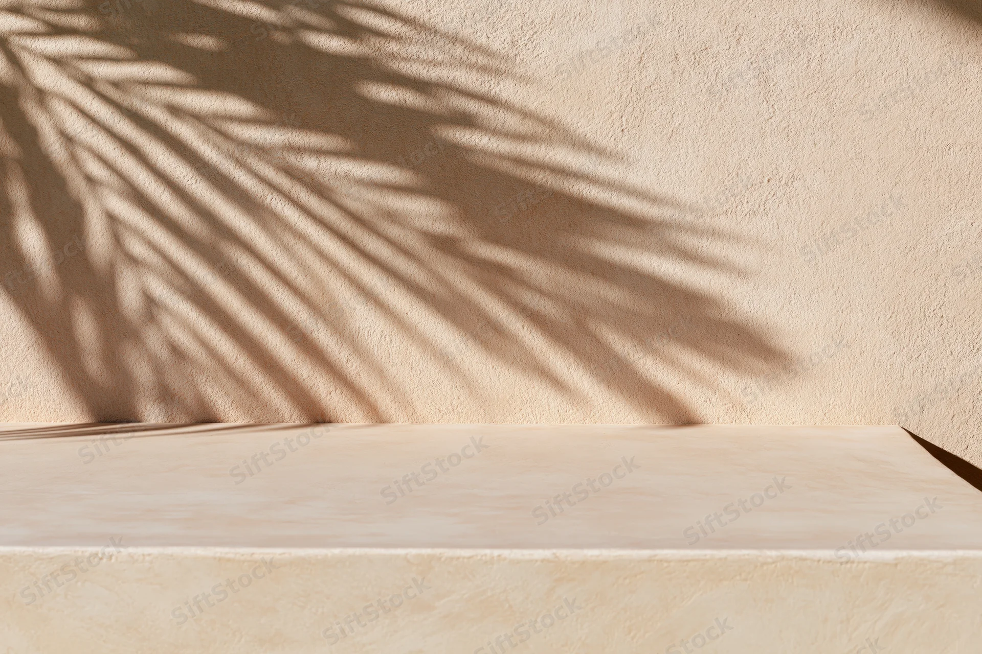 Shadow of palm leaf cast diagonally across beige textured wall above empty surface