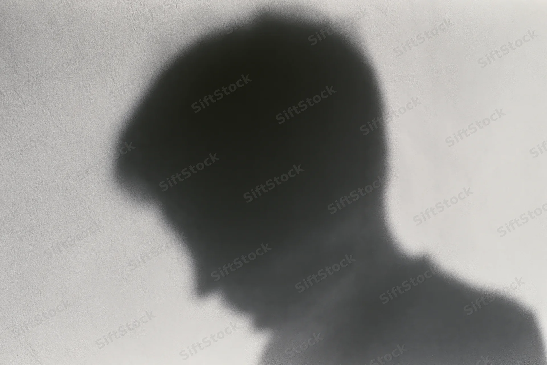 Shadow of a person looking downward cast on a pale concrete wall