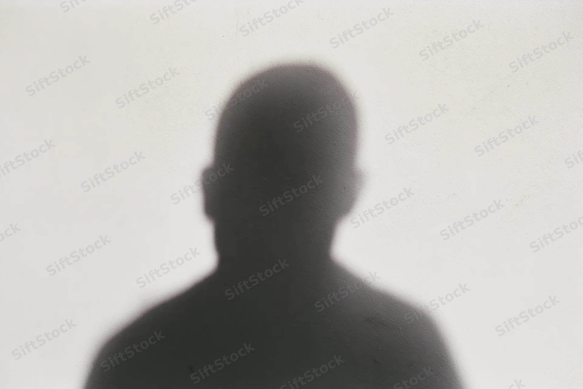 Shadow of a person cast on a pale concrete wall, looking downward