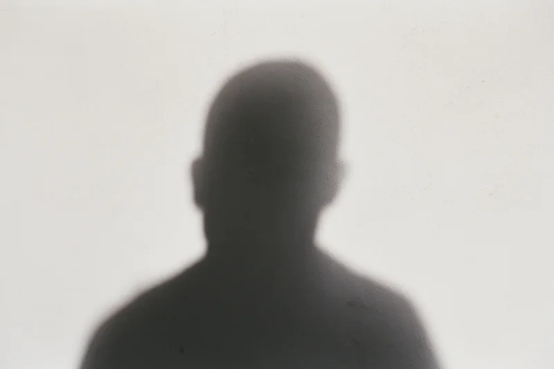 Shadow of a person cast on a pale concrete wall, looking downward