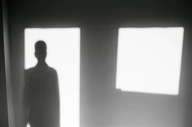 Shadow silhouette of a standing person projected onto a plain interior wall near a bright doorway