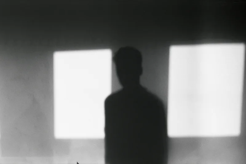 Silhouette of a standing person projected onto a plain interior wall between two bright windows