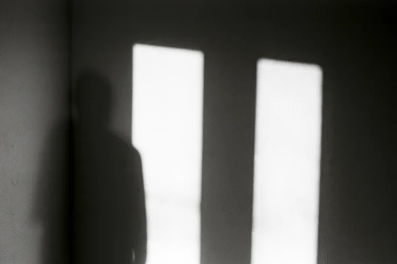 Shadow of a standing person cast on a dark wall beside two bright vertical light sources in an interior space