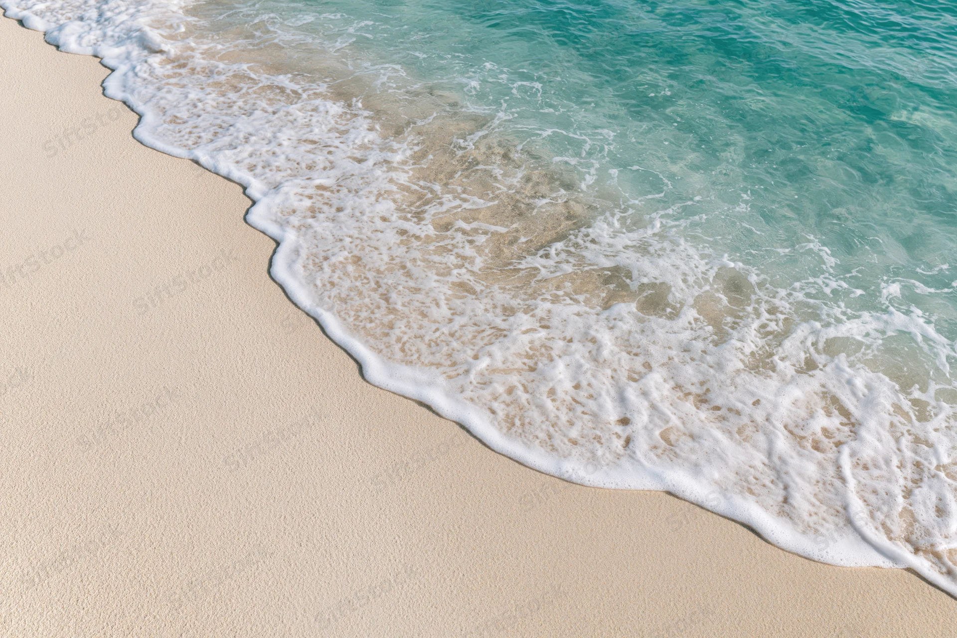 Shallow ocean wave gently washing over fine white sand at the beach