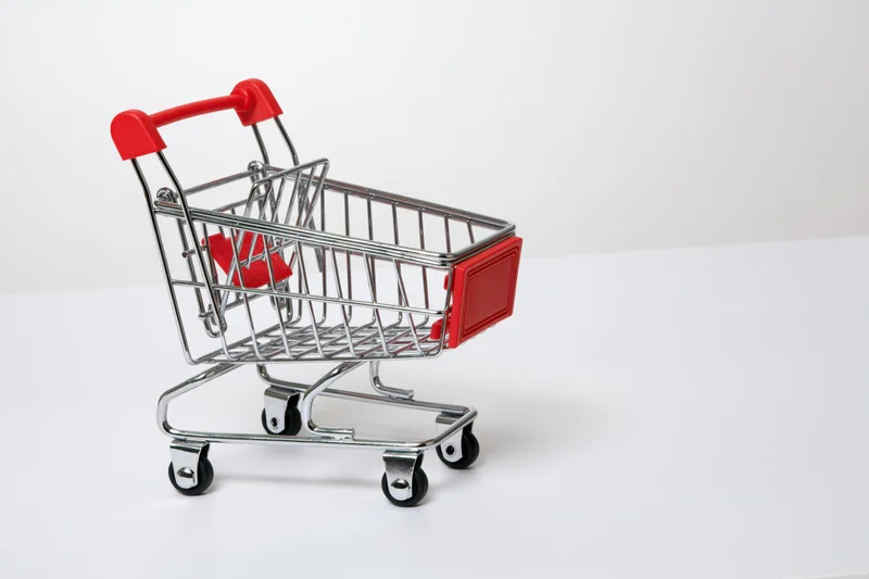 Miniature empty shopping cart with red plastic handle on white surface